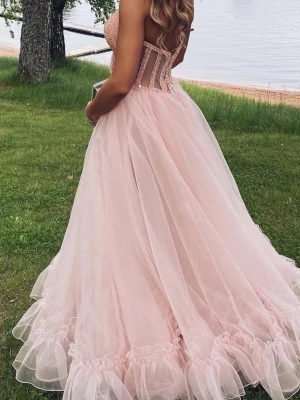 Ljusrosa balklänning med pärldetaljer - En drömmig ljusrosa balklänning med voluminös tyllkjol och axelbandslös överdel dekorerad med pärlor och paljetter. Livet har en snygg korsettlook med transparenta detaljer. Perfekt för bal. Korsett vilket gör att den passar olika storlekar 