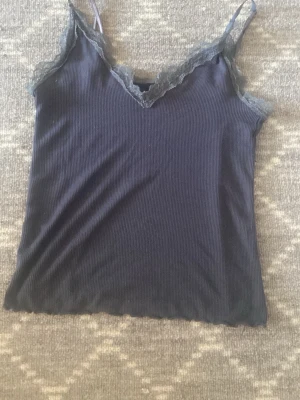 Mörkblå ribbad linnetopp från Amisu - Snygg mörkblå ribbad linnetopp från Amisu med spetsdetaljer längs v-ringningen och tunna axelband. Perfekt att styla med jeans eller kjol för en trendig look. Materialet känns mjukt och följsamt.