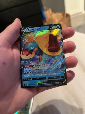 Pokémonkort Drednaw V japansk - Säljer ett japanskt Pokémonkort med Drednaw V-motiv. Kortet har en färgstark och glansig yta med blå, gul och röd design. Texten är på japanska och HP är 210. Perfekt för samlare eller Pokémonfans.