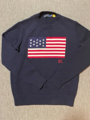 Stickad tröja från Ralph Lauren - Säljer denna riktigt snygga stickade tröja från Ralph Lauren med en amerikansk flagga och RL broderi på🇺🇸 Mycket bra skick 10/10, aldrig använd. Säljer då jag beställde fel storlek. Mitt pris: 700✅ Nytt pris: 1200❌ Priset är inte hugget i sten, kan ändras vid smidig affär
