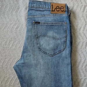 Blå raka jeans från Lee - Säljer ett par klassiska blå jeans från Lee med raka ben och fem fickor. Jeansen har en snygg tvättad look och Lee-logga på knapp och etikett. Tillverkade i slitstarkt denimtyg, perfekta för en avslappnad stil.