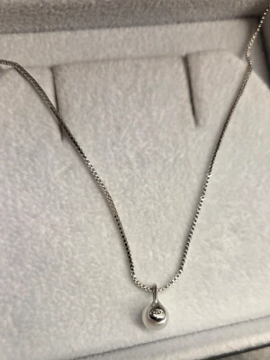 Silverhalsband med pärlberlock 925 - Snyggt halsband i silver med en rund, blank pärlberlock som hänger i en tunn kedja. Berlocken har en minimalistisk design och ger ett stilrent intryck. Perfekt för dig som gillar enkla men eleganta accessoarer. 925 ingraverat på hänget.