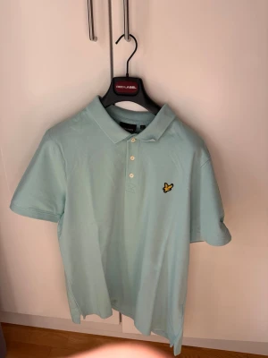 Lyle & Scott: Piké-tröja - Snygg ljusblå/turkos pikétröja från Lyle & Scott med klassisk krage och tre knappar framtill. Tröjan har det ikoniska gula logomärket broderat på bröstet och är tillverkad i mjuk bomull. Perfekt till jeans eller shorts för en clean look på sommaren! 🎉Piké-tröjan är köpt på Lyle&Scott’s outletbutik i Barkarby och är oanvänd därav utmärkt pris! 🎉För mer info skriv dm!