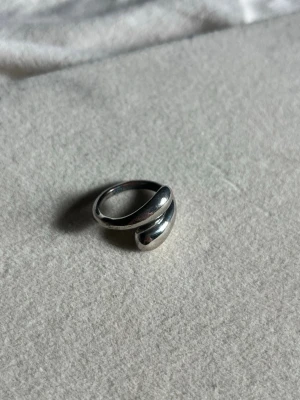 Chunky silverfärgad ring - Snygg chunky ring i silverfärgad metall med en modern, böjd design. Ringen har en blank yta och känns både stilren och trendig. Perfekt för dig som gillar minimalistiska accessoarer med lite edge.