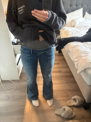 Blå bootcut jeans med slitningar - Säljer ett par blå bootcut jeans med lätt slitna detaljer på låret och knät. Jeansen har klassisk femficksdesign och normal midja. Perfekta för dig som gillar en avslappnad men ändå trendig look.