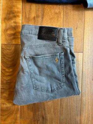 Grå jeans från Polo Ralph Lauren - Säljer ett par grå Polo Ralph Lauren jeans  Märke: Polo Ralph Lauren  Storlek: W30 L 30  Färg: Grå  Passform: Sullivan Slim Fit  Polo Ralph Lauren är sinnebilden av klassisk amerikansk "preppy"-stil, kända för sin tidlösa design och kompromisslösa kvalitet. Denna modell, Sullivan Slim, har en modern passform som sitter snyggt över benen utan att sitta för tajt.  Hör av dig!