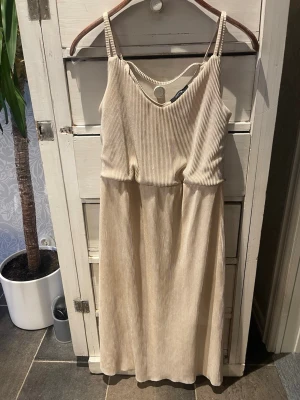 Beige ribbad långklänning - Snygg beige långklänning med smala axelband och v-ringning. Klänningen är ribbad och har en avslappnad passform som ger en skön känsla. Perfekt för varma dagar och enkel att styla med accessoarer.