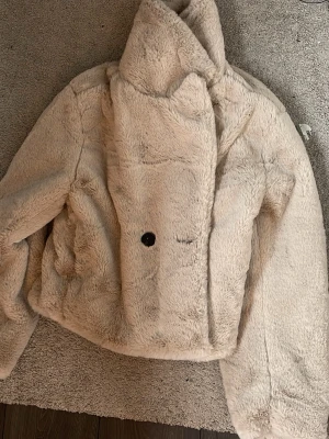 Beige teddyjacka  - Supermjuk teddyjacka i beige. Jackan har en dold knappstängning framtill och är helfodrad. Perfekt för dig som vill ha en cozy och trendig loook