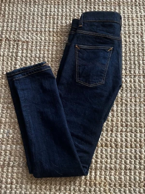 Nudie Grim Tim Dry True Navy - Saljer ett par superfina Nudie Jeans i modellen "Grim Tim". De är i den mörka och krispiga färgen "Dry True Navy", en klassisk rå denimblå färg med de karakteristiska orangea sömmarna.. Dessa jeans har en fantastisk potential att utveckla en helt unik slitning och patina över tid, eftersom de är i nyskick. Passa på att fynda ett par premiumjeans av hög kvalitet! Storleken är 30/34 men sitter som 29/34, pris nytt är runt 1700kr men jag släpper för endast 799kr! Vid frågor är det bara att skriva! 