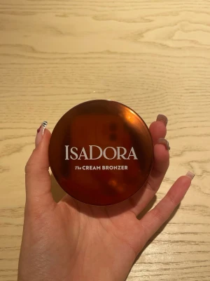 Isadora Cream Bronzer Medium - Krämig bronzer från Isadora i nyansen Medium. Kommer i en rund, brun kompakt dosa med spegel. Vegansk och parfymfri formula som ger en naturlig solkysst look. Perfekt för att skulptera och ge värme till ansiktet.