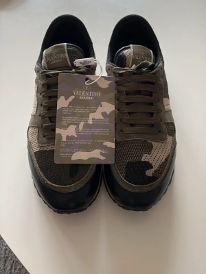 Valentino Garavani camo sneakers - Snygga sneakers från Valentino Garavani med kamouflagemönster i grönt, beige och svart. Medföljer extra skosnören, certifikat och dustbag. Perfekta för dig som gillar och exklusiva märken.