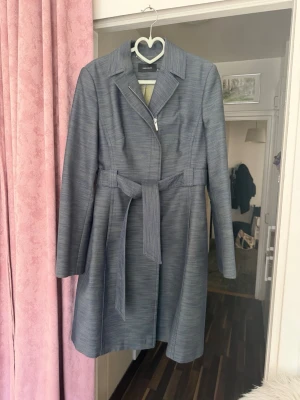 Karen Millen grå kappa med bälte NY – storlek EU 40 (UK 12) - Karen Millen grå kappa med bälte – storlek EU 40 (UK 12) NY  Elegant och figursydd kappa från Karen Millen i grå färg. A-linjeform med bälte som ger en väldigt smickrande passform. Tyg i hög kvalitet med inslag av silke som håller formen fint. Passar både till vardag och mer uppklätt.  • Märke: Karen Millen • Storlek: EU 40 / UK 12 / US 8 • Färg: grå • Med bälte • Dragkedja framtill • Skick: mycket fint skick • Material: bomull, polyamid, silke, polyester (foder: viskos/acetat)