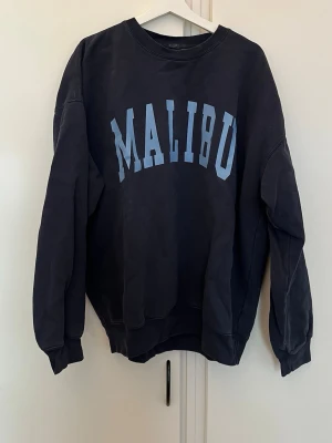 Sweatshirt  - Säljer en mörkblå sweatshirt från Brandy Melville med  ljusblått 'Malibu'-tryck på framsidan i storlek onesize. Använd ett fåtal gånger men bra skick!! 🙌🏽
