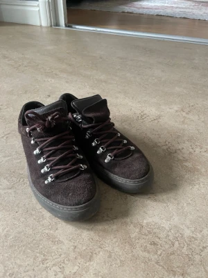 Diemme - Mörkbruna sneakers i mocka med robusta bruna snören och metallhakar för snörningen. Skorna har en låg profil och en tjock, mörk sula. Perfekta för dig som gillar en stilren men ändå lite rugged look.
