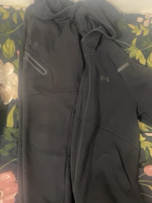 Svarta mjukisbyxor från Under Armour - Säljer ett par svarta mjukisbyxor från Under Armour med elastisk midja och dragkedjeficka på sidan. Byxorna har en sportig look med diskret logga och är tillverkade i ett mjukt, stretchigt material som passar perfekt för chill eller träning.