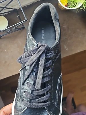 Svarta sneakers från Pull&Bear - Stilrena svarta sneakers från Pull&Bear med vita sulor och svarta skosnören. Skorna har en klassisk låg design i konstläder med diskreta sömmar och en bekväm passform. Perfekta för en avslappnad och trendig look.