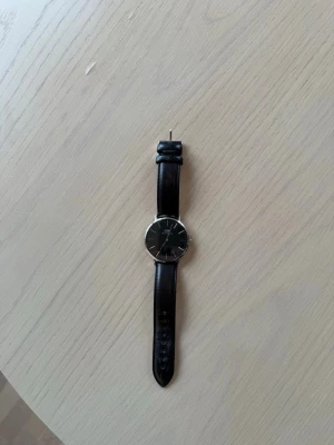Daniel Wellington klocka svart läder - Stilren klocka från Daniel Wellington med svart urtavla och silverfärgat boett. Armbandet är i svart läder och har klassisk design. Perfekt accessoar för dig som. Levereras i originalask. Endast använd enstaka gånger. 