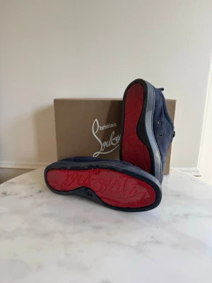 Mörkblå Christian Louboutin  - Snygga mörkblå sneakers från Christian Louboutin med klassisk röd sula och diskret logga undertill. Skorna har en låg profil, rund tå och är tillverkade i mocka med matchande mörkblå snörning. Perfekta för dig som vill sticka ut med exklusiva detaljer. Obs innersula saknas. Pris går stt diskuteras!