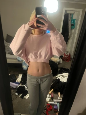 Ljusrosa cropped hoodie - Säljer en ljusrosa cropped hoodie med breda ärmar och ribbade muddar. Tröjan har en avslappnad passform och är tillverkad i mjukt sweatshirt-material. Perfekt för dig som gillar en chill och trendig look.