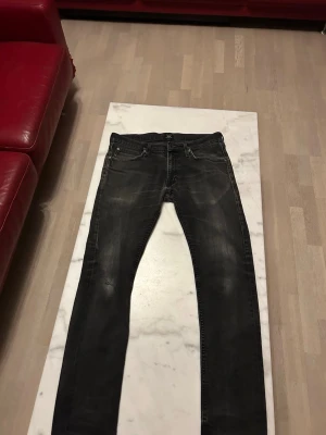 Svarta slim fit jeans från Lee - Snygga svarta slim fit jeans från Lee med slitna detaljer och klassisk femficksdesign. Jeansen har en något tvättad look och är tillverkade i denim med stretch för extra komfort. Perfekta för en avslappnad och trendig stil.