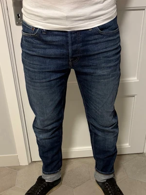 jeans från Jack&Jones - Säljer ett par mörkblå jeans från Jack&Joned med klassisk rak passform och fem fickor. Jeansen har diskreta slitningar och uppvikta benslut för en avslappnad look. Perfekta till sneakers och t-shirt. Materialet är denim i bomull. Hör av dig vid minsta intresse!✨💫⭐️