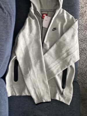 Gråa mjukisbyxor från Nike - Snygga gråa mjukisbyxor från Nike med svarta dragkedjor vid fickorna och liten Nike-logga på benet. Byxorna har en avslappnad passform och är tillverkade i mjukt material som passar perfekt för chill eller träning.