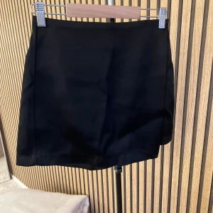 Svart skort från H&M - Stilren svart skort med rak passform och slät framsida. Klassisk look som passar till många olika stilar. Materialet ser ut att vara ett mjukt tyg med lätt struktur. Perfekt för dig som vill ha både kjolens look och shortsens komfort.