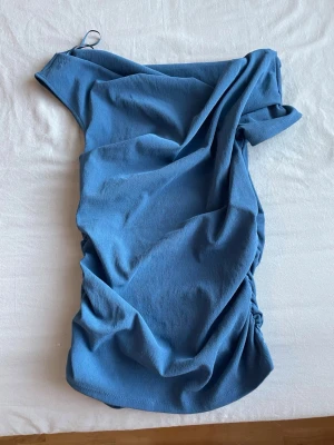 Blå offshoulder topp - Trendig blå topp med offshoulder-design och rynkade detaljer på sidan. 