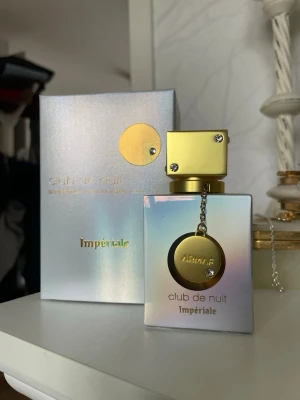 Armaf Club de Nuit Impériale parfym 30ml edp - Säljer en lyxig parfym från Armaf, Club de Nuit Impériale. Flaskan har en skimrande, pärlemorfärgad finish med gulddetaljer och en dekorativ medaljong i kedja. Förpackningen matchar flaskans eleganta design. Perfekt för dig som gillar exklusiva dofter. Testat ett spray!