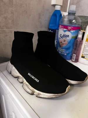  Speed Trainer svarta sneakers - Svarta Speed Trainer sneakers med stickad strumpdesign och tjock vit sula. Skorna har B logga på sidan och är tillverkade i stretchigt textilmaterial som formar sig efter foten. Perfekta för dig som gillar streetwear och vill ha något riktigt trendigt.