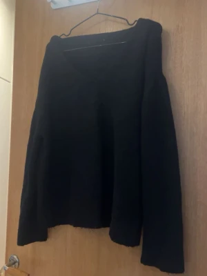 Svart stickad tröja med v-ringning - En enkel och stilren svart stickad tröja med v-ringad hals och långa ärmar. Tröjan har en lös passform och är perfekt för lager på lager. Passar till det mesta och är ett måste i garderoben.