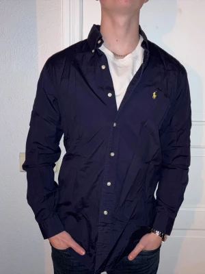 Mörkblå skjorta från Ralph Lauren - Mörkblå skjorta från Ralph Lauren i storlek M.  Fint skick till ett bra pris. Nypris: 1995kr. Mitt pris: 349kr. Vid frågor eller funderingar, tveka inte att höra av dig.
