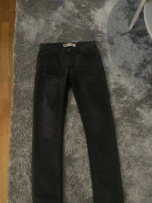 Svarta jeans från Levi's - Säljer ett par svarta jeans från Levi's med klassisk femficksdesign och knappgylf. Jeansen har en smal passform och är tillverkade i stretchigt denimtyg för extra komfort. Perfekta till en avslappnad streetstyle-look.