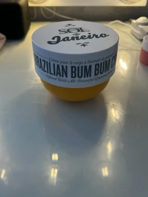 Sol de Janeiro Brazilian Bum Bum Cream - En ikonisk kroppskräm från Sol de Janeiro i en rund, gul burk med vitt lock. Brazilian Bum Bum Cream har en krämig konsistens och doftar tropiskt. Perfekt för att återfukta huden och ge en silkeslen känsla.
