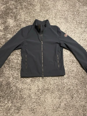 Colmar jacka - Snygg mörkblå softshelljacka från Colmar i storlek Small(46). Jackan har en krage och två dragkedjeförsedda fickor framtill. Jackan har en diskret logotyp på ärmen och baktill, men även en snygg text vid dragkjedjan. Tillverkad i ett lätt och smidigt material som passar perfekt under vår, sommar och häst. Jackan är urvuxen och ändast använd en säsong. 