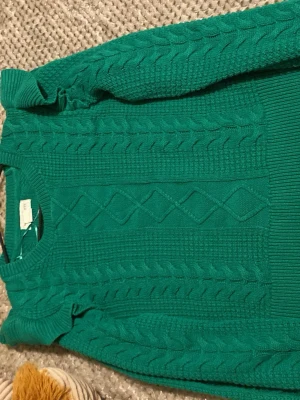 Grön kabelstickad tröja - Säljer en snygg grön kabelstickad tröja med rund hals och klassiskt flätmönster framtill och på ärmarna. Tröjan har ribbade muddar och är perfekt för dig som gillar en stilren men ändå trendig look.
