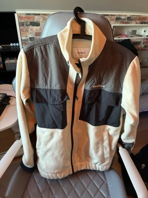 Beige fleecejacka från Woodbird - Säljer en beige fleecejacka från Woodbird med svarta detaljer och bröstfickor. Jackan har hög krage, hel dragkedja och kontrastpaneler i mörkgrått. Perfekt för lager-på-lager och chill stil. Storlek xs men sitter som s