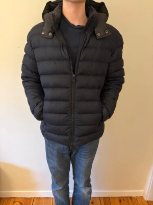 Svart mörkblå jacka från Colmar - Säljer en mörkblå pufferjacka från Colmar med huva och dragkedja framtill. Jackan har ett klassiskt quiltat mönster och Colmar-logga på ärmen. Perfekt för kalla dagar och har en modern, sportig look. Storlek 52 står det i den, sitter som en liten M eller en stor S. Perfekt för dig mellan 170-175cm!