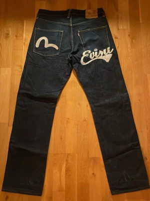 Mörkblåa Evisu Jeans - Mörkblåa Evisu Jeans i storlek 34! Dom har text på baksidan av byxorna och är i mycket bra skick! Midjemått: 40cm. Längd: 103cm. Innerbenslängd: 78cm. Pris kan diskuteras🥰