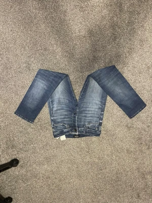 Blå slim fit jeans SLIM/GLENN - Snygga blå slim fit jeans i modellen SLIM/GLENN med klassisk femficksdesign och lätt slitna detaljer. Jeansen har normal midja och raka ben, perfekta till vardagslooken. Tillverkade i mjukt denimtyg för skön känsla.