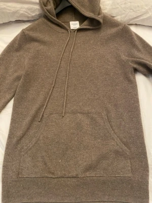 John Henric beige Kashmir  - Mjuk och lyxig beige hoodie från john Henric i cashmere. Klassisk modell med huva och magficka framtill. Tröjan är i strl S. Tröjan är i bra skick förutom ett jätte litet hål som visas på bild 4,5 och de märks inte av och syns inte vid användning.