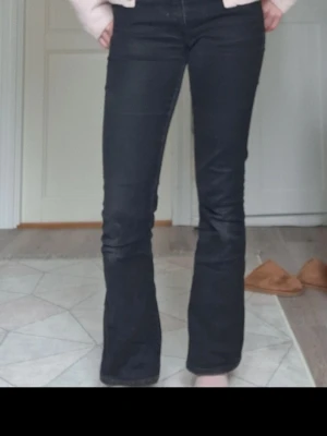 Svarta bootcut jeans från Croker - Säljer ett par svarta bootcut jeans från Croker med klassisk femficksdesign och knappgylf. Jeansen har en snygg passform med lätt utsvängda ben och är tillverkade i ett mjukt denimtyg som är bekvämt att bära. Stl 27/31. De är lite korta för mig som är 169cm. Lite slitna vid knäna men inte något hål eller så, bara förlorat färgen lite men inet som syns tydligt på! De är inte jätte utsvängda, men ändå bootcut.