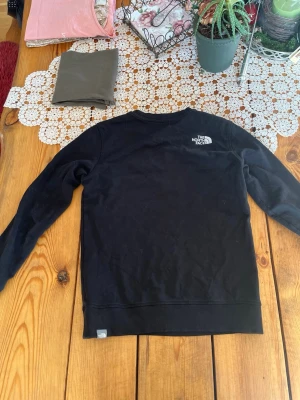 Svart North face tröja - Tröjan är i bra skick förutom ett litet hål i mitten som jag sytt ihop. Arnas ör det skön och har en ”slim fit”