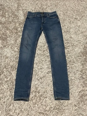 Blå slim jeans - Säljer ett par Blå slim jeans med klassisk femficksdesign och smal passform. Jeansen har diskreta slitningar framtill och kontrastsömmar. Perfekta till sneakers eller boots för en clean look.