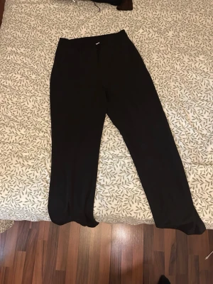 Svarta kostymbyxor med rak passform - Snygga svarta kostymbyxor med rak passform och hög midja. Byxorna har bälteshällor och en diskret bakficka. Perfekta till en stilren look och passar till skjorta eller t-shirt. OBS! Kan förekomma katthår på detta plagg säljs där av billigare…