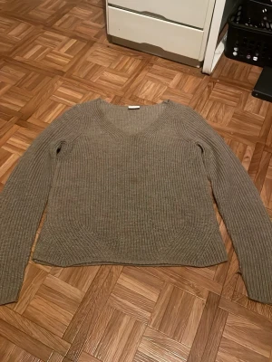 Olivgrön ribbstickad tröja - Säljer en olivgrön ribbstickad tröja med v-ringning och långa ärmar. Tröjan har en avslappnad passform och är perfekt för lager på lager. Materialet känns mjukt och bekvämt, och den ribbade strukturen ger en snygg touch till outfiten.