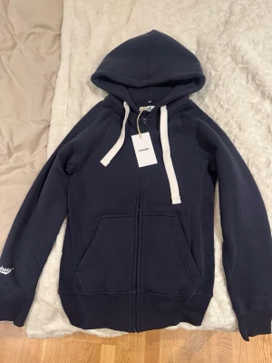 Mörkblått set Russemearch, nyskick - Mörkblå hoodie från Russemearch med dragkedja, stora fickor framtill och vita, breda dragsnören i huvan.                           Är helt och hållet oanvänd inte ens testade. Så helt nyskick!    Byxor: XXS Tröja:XS.   Nypris: 1248kr så bra pris för helt nytt sett! ✅