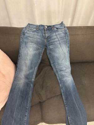 Blå bootcut jeans från 7 For All Mankind - Snygga blå bootcut jeans från 7 For All Mankind med klassisk femficksdesign och ljusa slitningar framtill. Jeansen har låg midja och är tillverkade i mjuk denim med lite stretch för extra komfort. från 2000  midjemått 42,5/43