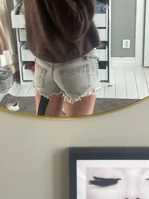 Gråa jeansshorts med fransar - Säljer ett par ljusgrå jeansshorts med råa, fransiga kanter och klassiska bakfickor. Shortsen har låg midja och en avslappnad passform. Perfekta för varma dagar, 💕