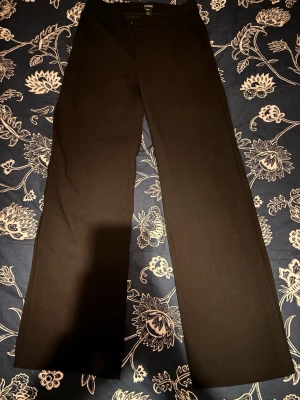 Svarta kostymbyxor från Lindex - Snygga svarta kostymbyxor från Lindex med raka ben och klassisk passform. Byxorna har hällor för skärp och diskreta fickor framtill. Perfekta för en stilren och clean look. Materialet känns mjukt och har en lätt stretch för extra komfort.